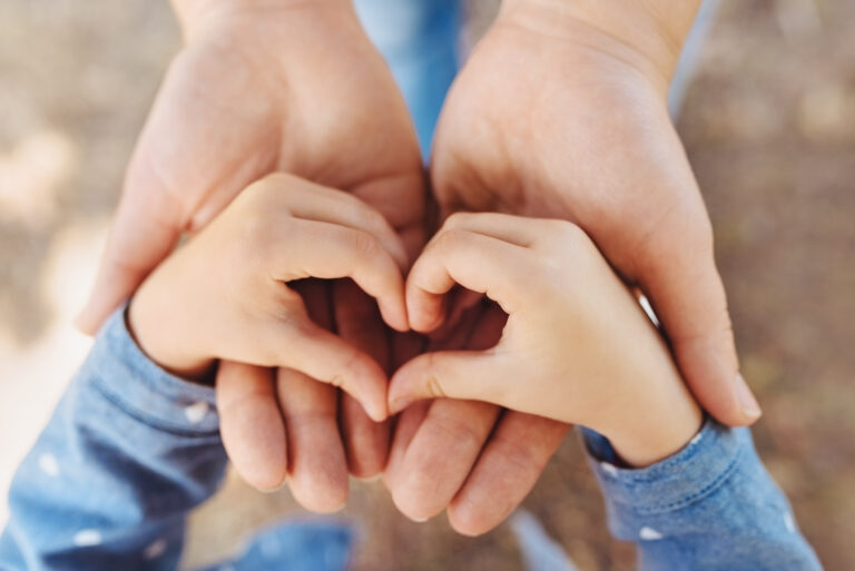 Concept Happy Mother's Day or International Day of Families. Close-up of child's hands showing shape of heart in hands of mother. Sign of love and happiness. Greeting card. Top view.